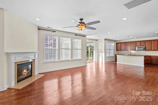 a view of an empty room with wooden floor and a kitchen