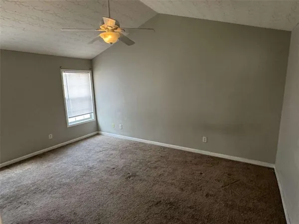 an empty room with chandelier fan and windows