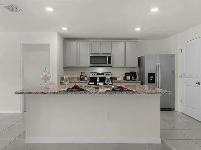 a kitchen with stainless steel appliances a sink a stove a refrigerator a center island and cabinets