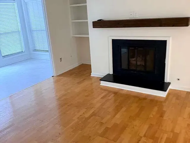 a view of an empty room with wooden floor and a fireplace