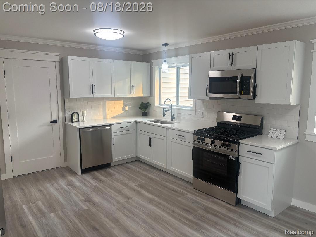 32563 Sutton Road New Baltimore, MI 48047 - Photo 18 of 43 Modern kitchen featuring white shaker cabinetry, stainless steel appliances, white subway tile backsplash, light wood-finish flooring, and solid surface countertops