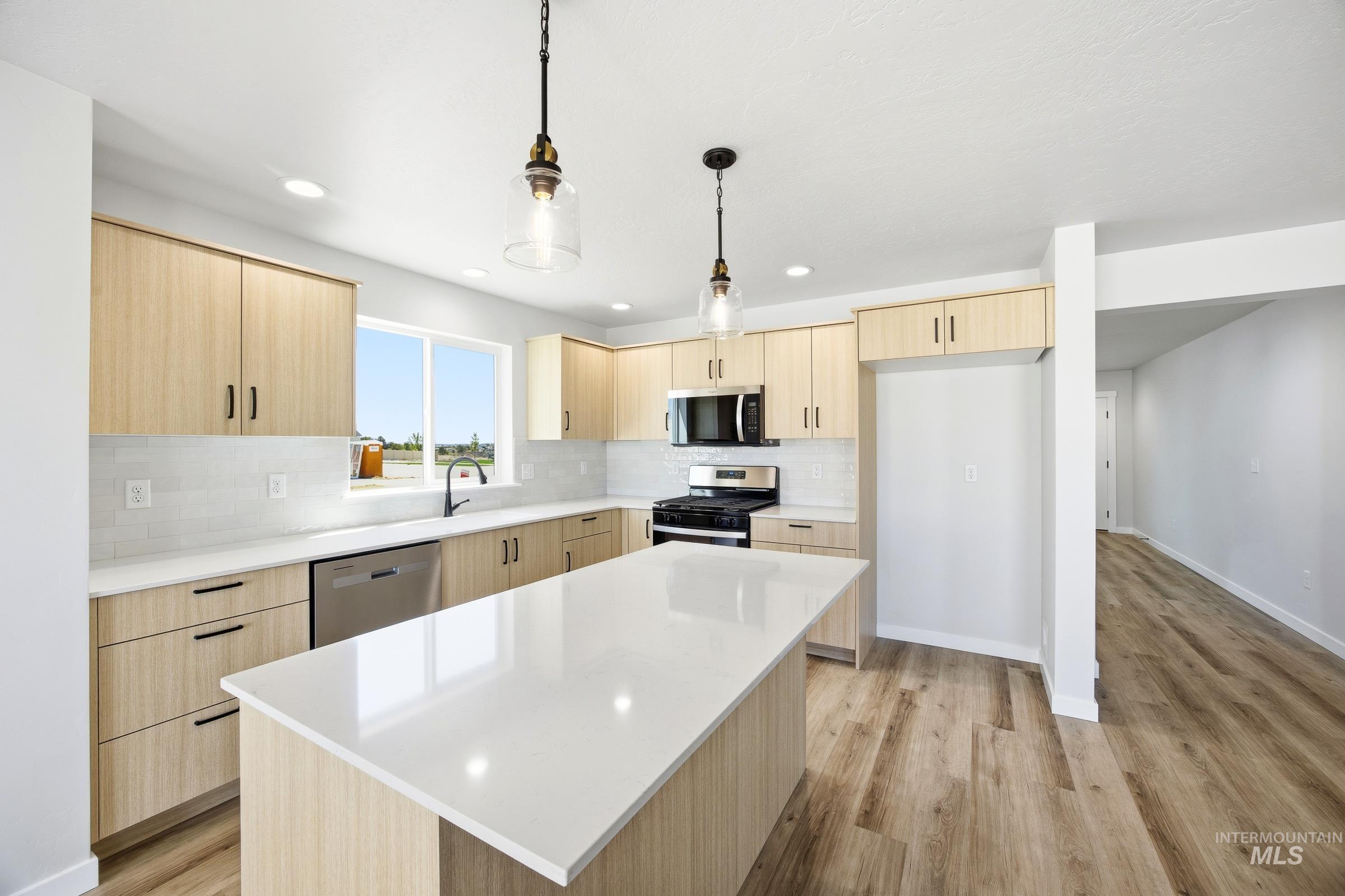 12841 Decatur Street Nampa, ID 83651 - Photo 4 of 30 Kitchen featuring an expansive center island with a light-toned countertop, wood-finish cabinetry, stainless steel appliances, and wood-finish flooring