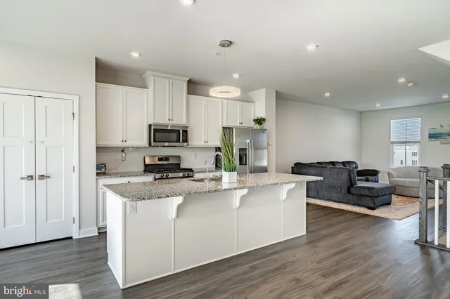 a living room with stainless steel appliances granite countertop wooden floor a couch and a window