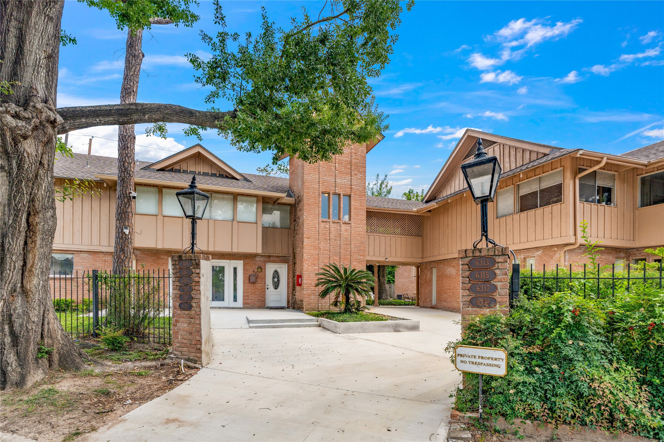 6303 Crab Orchard Road, Unit 3 Houston, TX 77057 - Photo 2 of 30 Step onto the property and be greeted by a sophisticated blend of classic red brick and modern siding. The grand entrance is anchored by stately brick pillars topped with traditional lanterns, framing a pristine concrete driveway. The lush, mature landscaping and soaring trees provide an immediate sense of privacy and established luxury.