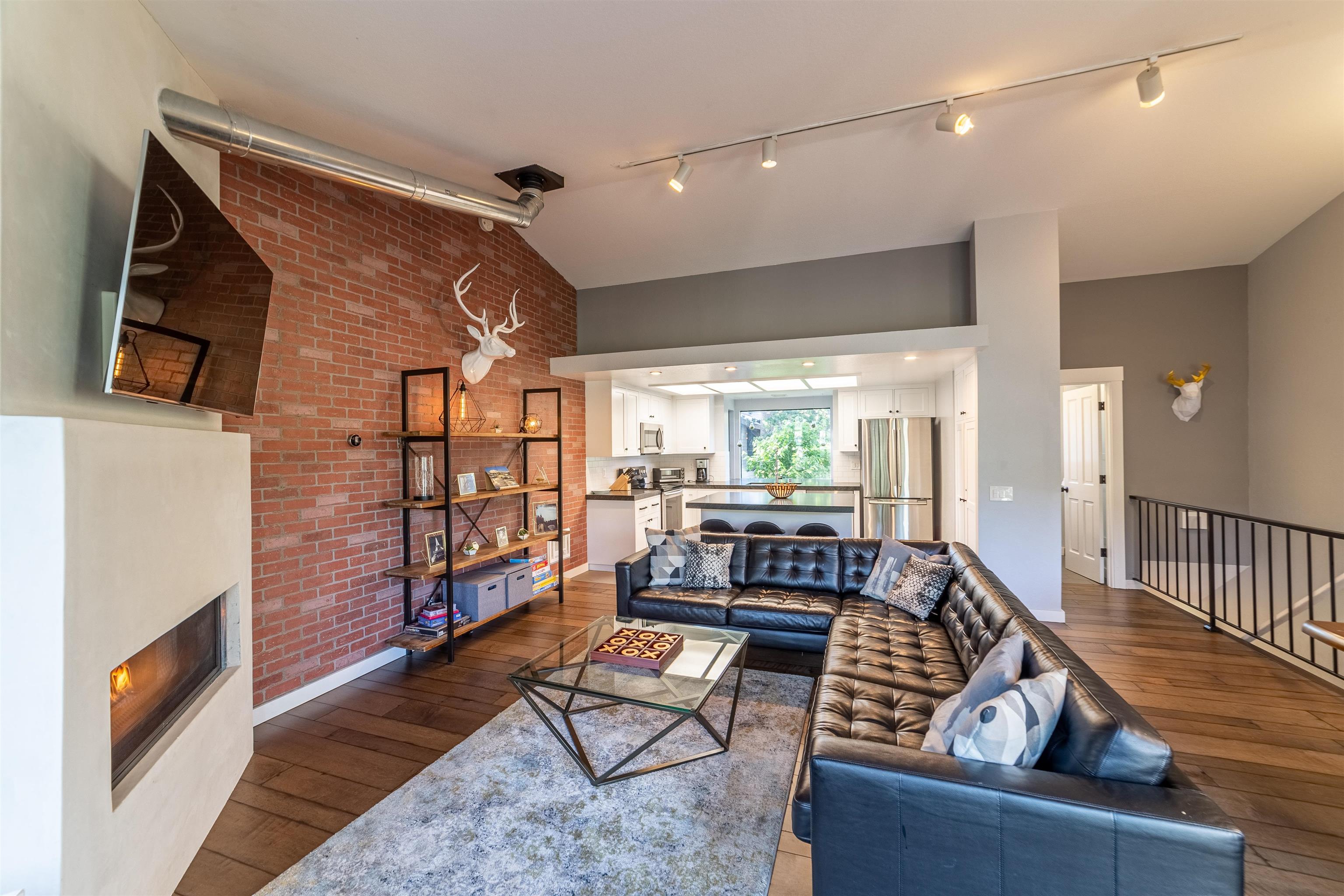 384 Joaquin Road, Unit 31 Mammoth Lakes, CA 93546 - Photo 1 of 29 Living room featuring track lighting, dark wood finished floors, lofted ceiling, brick wall, and a warm lit fireplace