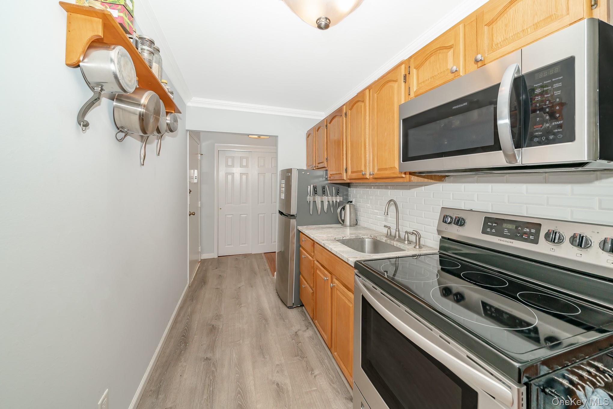 2449 F Union Boulevard, Unit 12A Islip, NY 11751 - Photo 11 of 16 Kitchen with appliances with stainless steel finishes, crown molding, light wood-style flooring, light stone counters, and tasteful backsplash