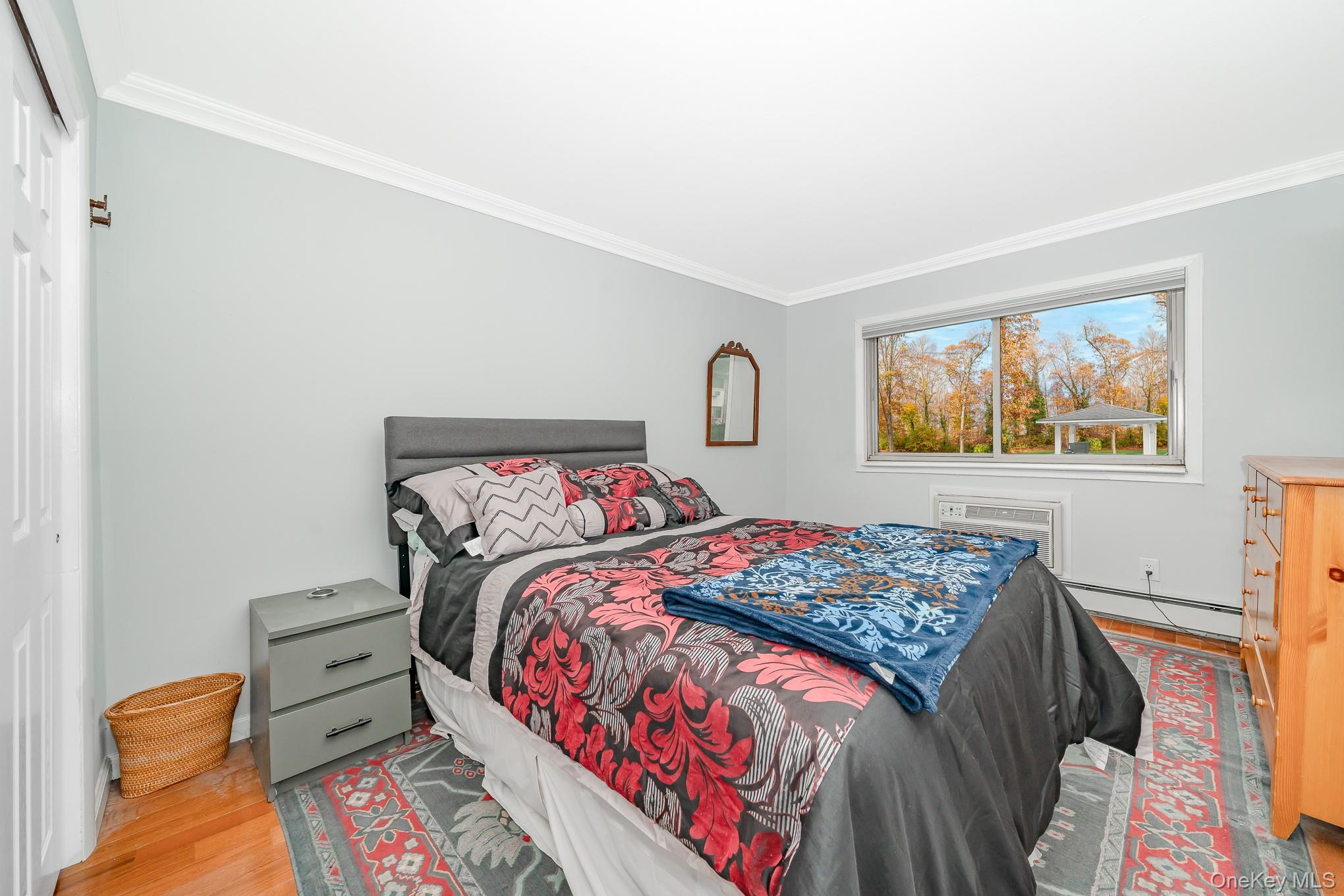 2449 F Union Boulevard, Unit 12A Islip, NY 11751 - Photo 12 of 16 Bedroom featuring crown molding, a baseboard heating unit, wood finished floors, a wall unit AC, and a closet