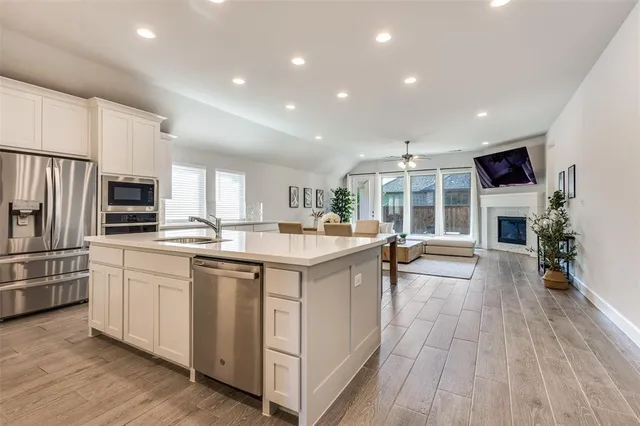 a kitchen with stainless steel appliances granite countertop a refrigerator oven a sink dishwasher and white cabinets with wooden floor