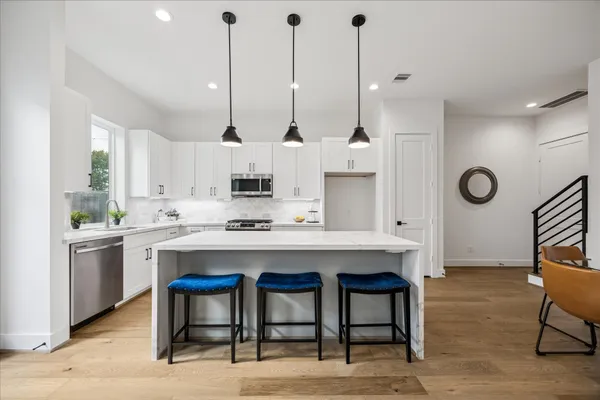 a kitchen with stainless steel appliances granite countertop a stove a sink a dining table and chairs with wooden floor