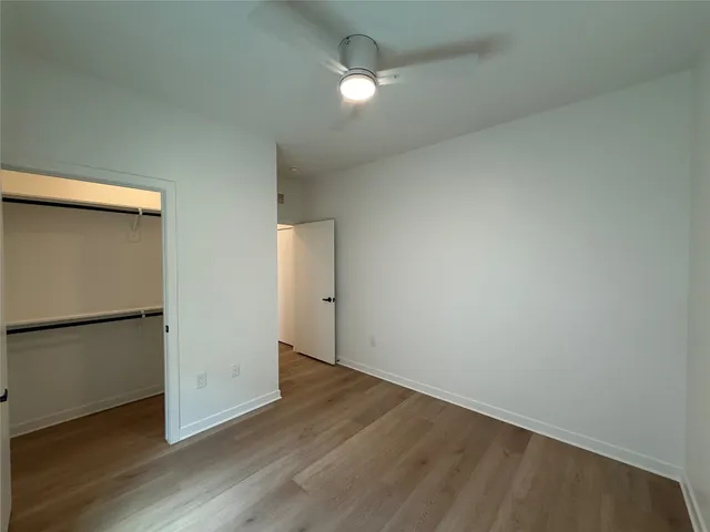 an empty room with wooden floor a ceiling fan and windows