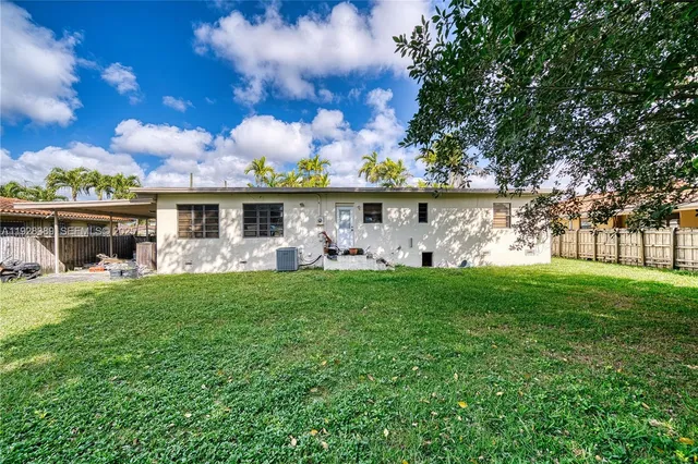 a view of a white house in front of a big yard with plants and large trees