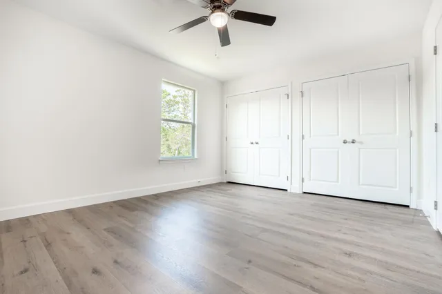 an empty room with wooden floor ceiling fan and windows