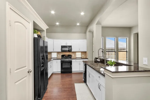 a kitchen with stainless steel appliances granite countertop a refrigerator a sink dishwasher a stove and a dining table with wooden floor