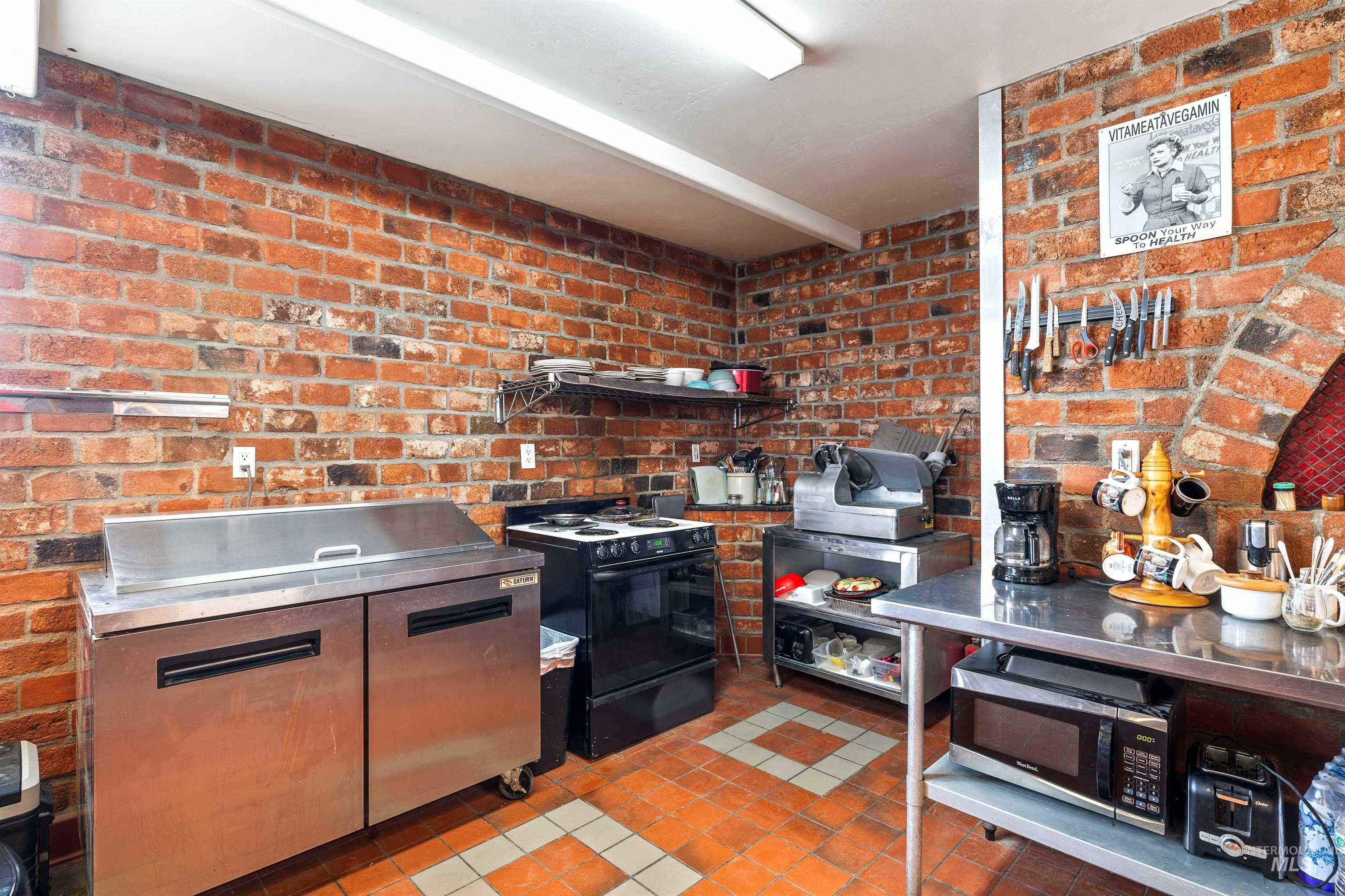 2039 Main Street Gooding, ID 83330 - Photo 12 of 31 Kitchen featuring stainless steel countertops, brick wall, tile patterned flooring, black range with electric cooktop, and stainless steel microwave