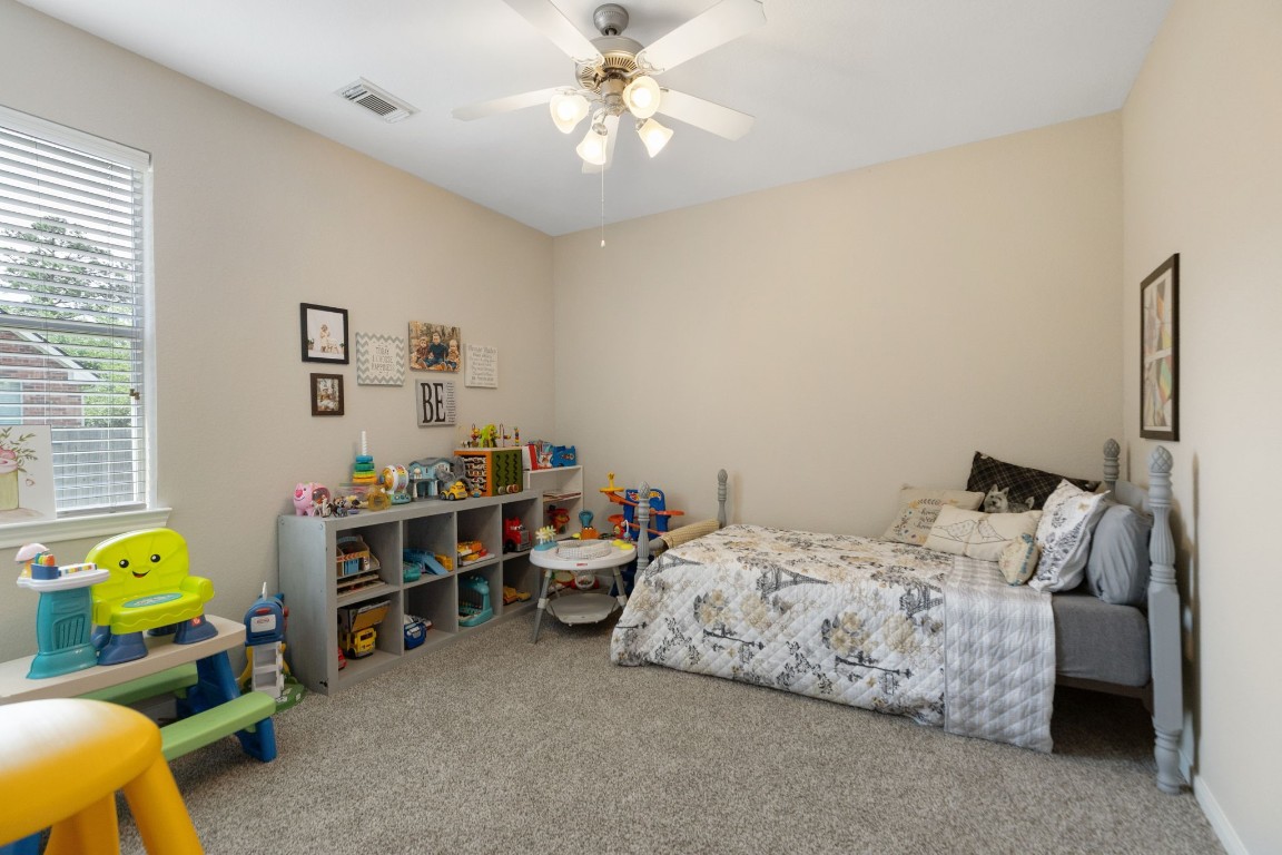 20410 Misty Crossing Lane Spring, TX 77379 - Photo 27 of 50 This cozy bedroom features a soft, neutral color palette with a comfortable bed and a ceiling fan. A window provides natural light, and a well-organized shelving unit.