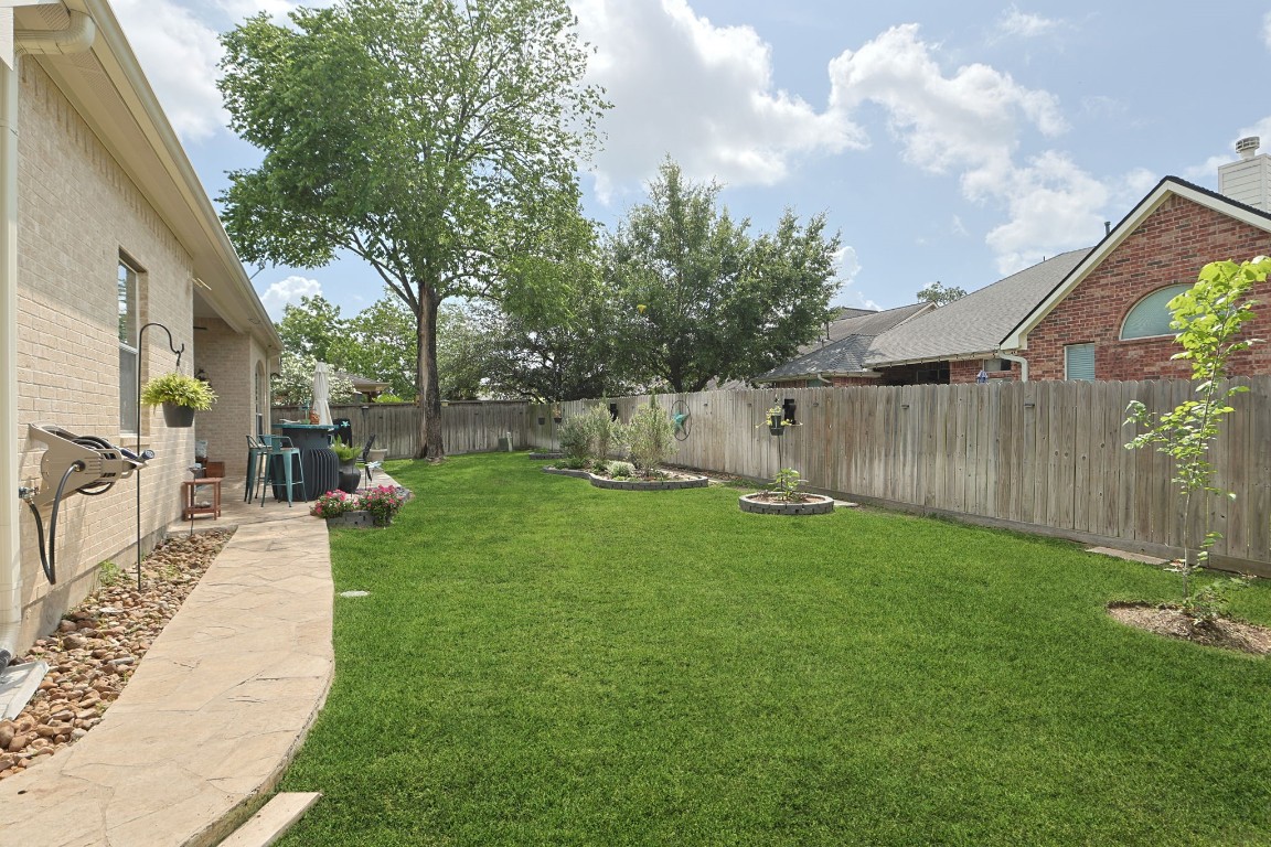 20410 Misty Crossing Lane Spring, TX 77379 - Photo 34 of 50 A spacious backyard featuring a well-maintained lawn, a paved walkway, and mature trees. The area is bordered by a wooden fence and includes landscaped flower beds, perfect for outdoor activities and relaxation.