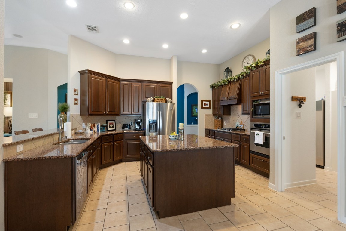 20410 Misty Crossing Lane Spring, TX 77379 - Photo 9 of 50 This spacious kitchen features rich wood cabinets, granite countertops, and a central island. It includes modern stainless steel appliances, recessed lighting, and tile flooring, providing a warm and functional space for cooking and entertaining.