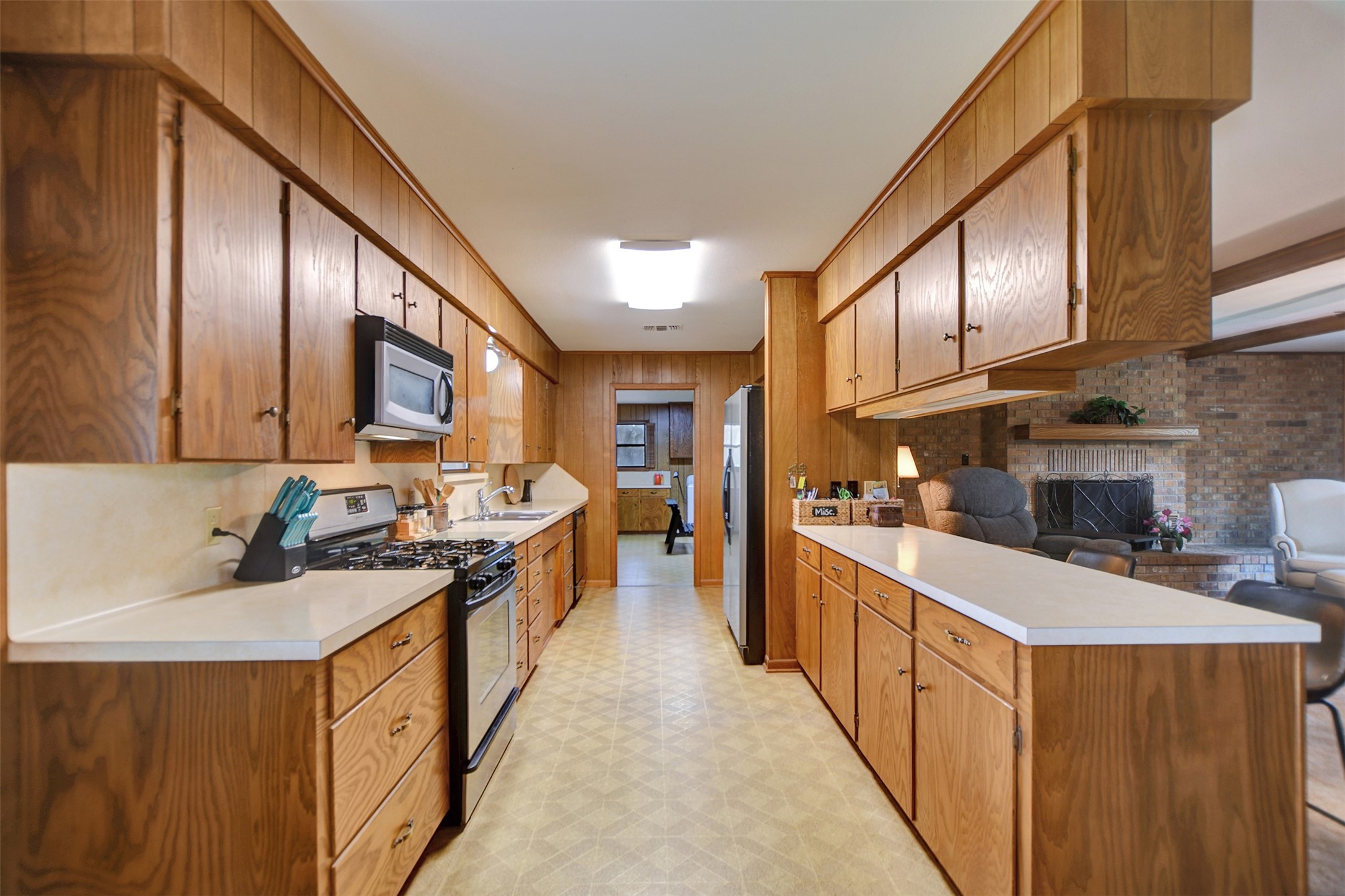 341 South S Loop Bellville, TX 77418 - Photo 11 of 33 This spacious kitchen features ample wooden cabinetry, modern stainless steel appliances, and a cozy adjoining living area with a brick fireplace, ideal for entertaining and gatherings.