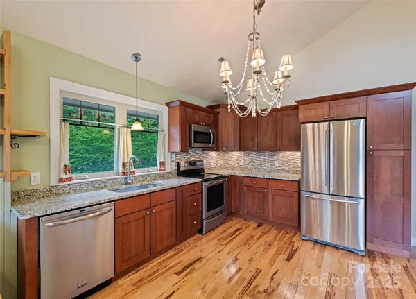 a kitchen with stainless steel appliances granite countertop a refrigerator a sink dishwasher a kitchen island with wooden floor and chandelier