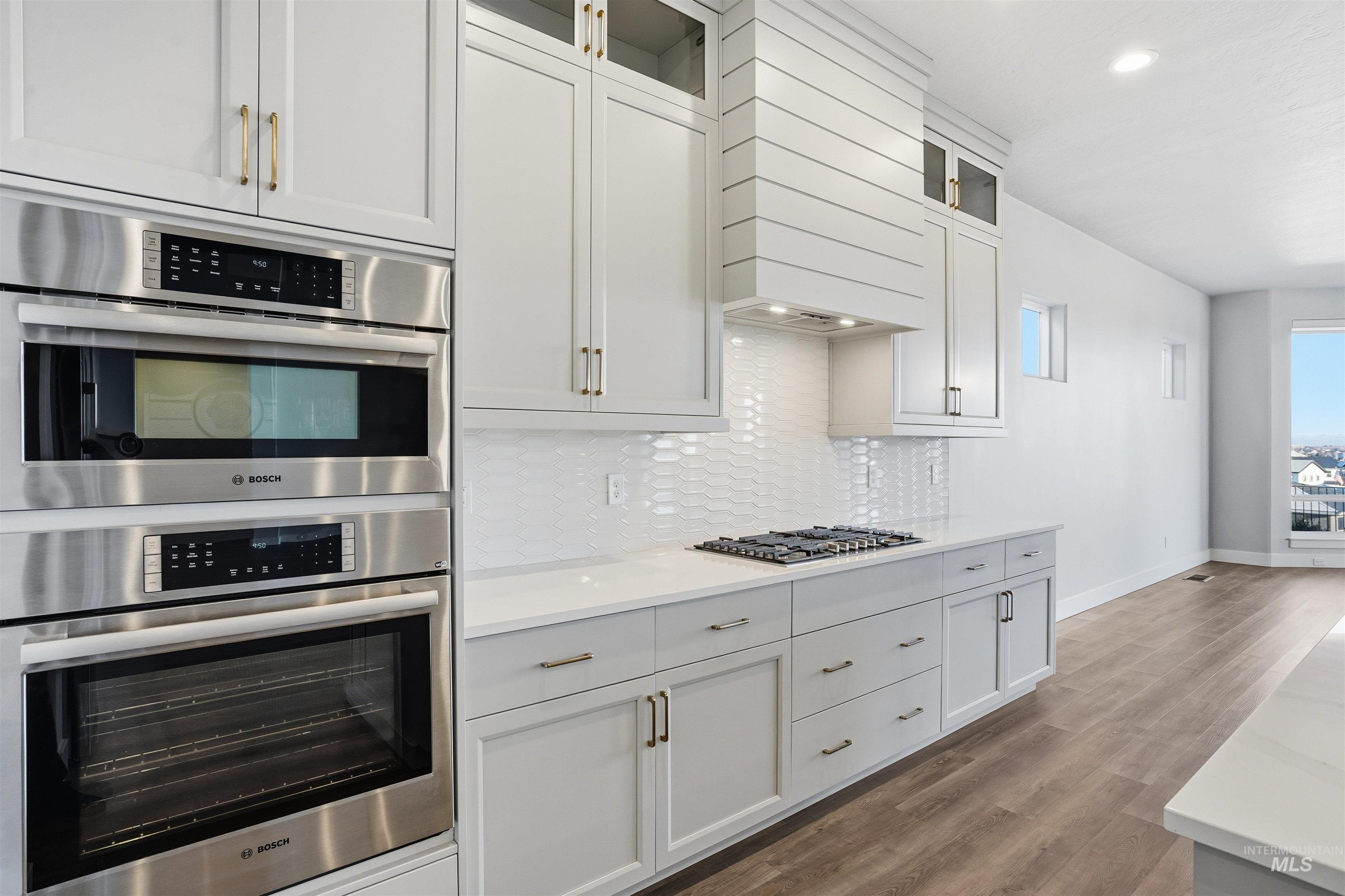 2976 East Parulo Drive Meridian, ID 83642 - Photo 13 of 40 Kitchen featuring stainless steel appliances, glass insert cabinets, dark wood-type flooring, light stone countertops, and white cabinetry