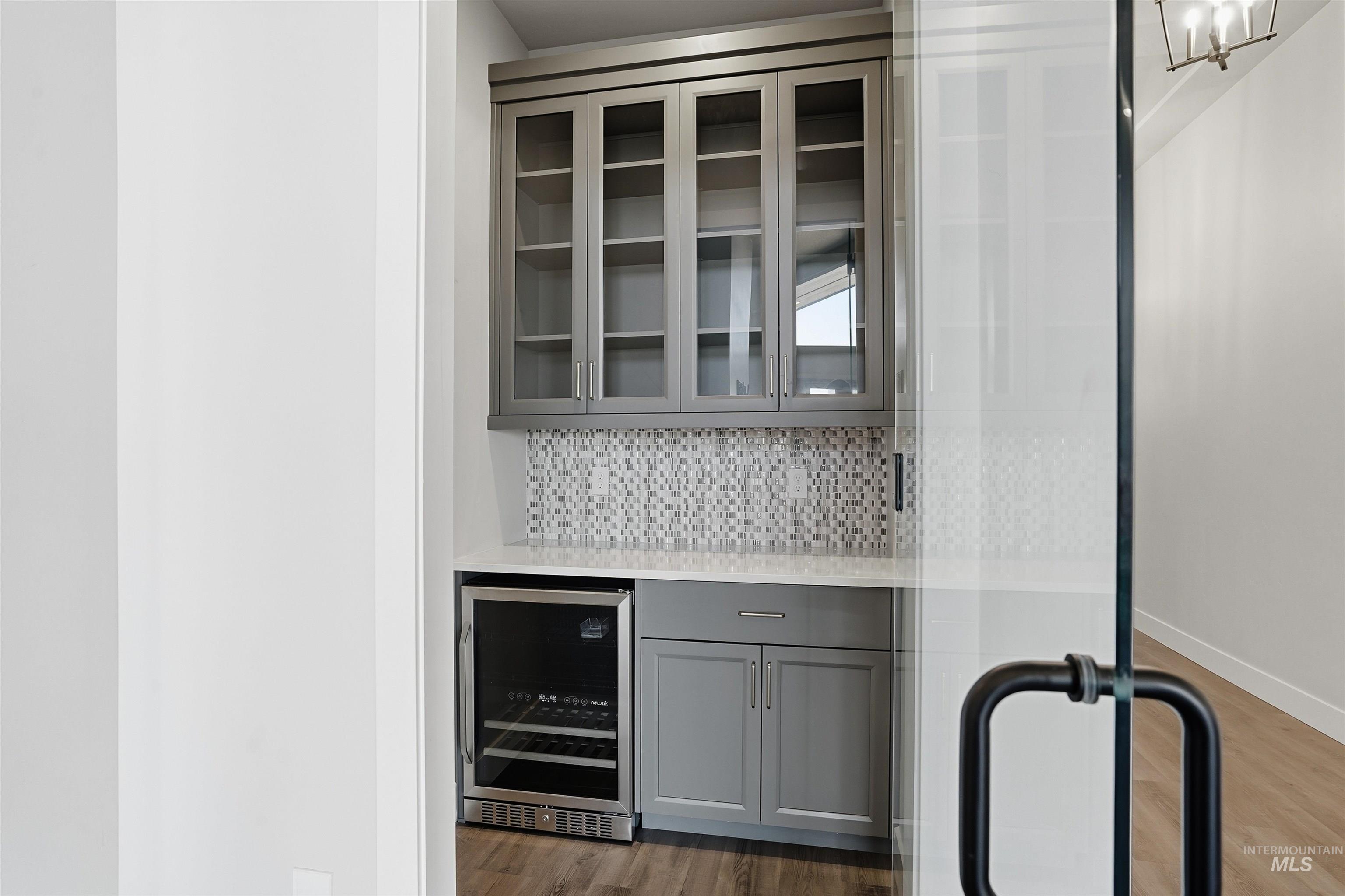 2976 East Parulo Drive Meridian, ID 83642 - Photo 10 of 40 Indoor dry bar featuring gray cabinetry, beverage cooler, decorative backsplash, light stone counters, and glass insert cabinets
