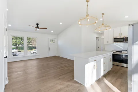 a large kitchen with granite countertop a stove a sink a center island and wooden floor