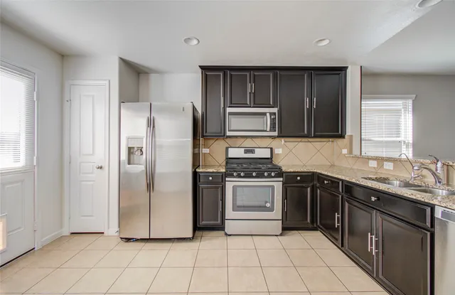 a kitchen with stainless steel appliances granite countertop a stove top oven a sink and a refrigerator
