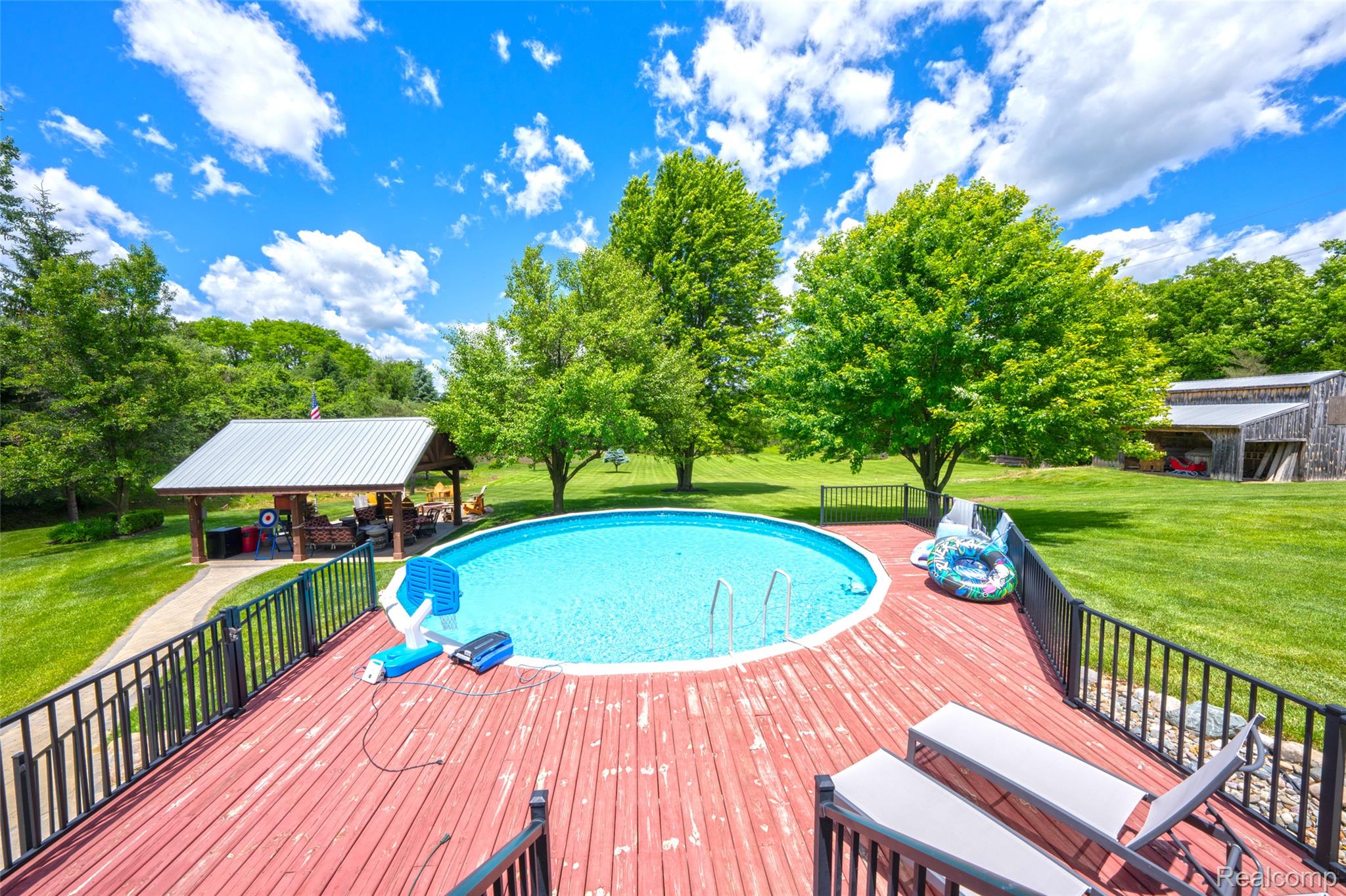 5233 Crawford Road Dryden, MI 48428 - Photo 12 of 95 Expansive outdoor space featuring a large wooden deck with black metal railing, an above-ground pool, and a covered pavilion with a metal roof