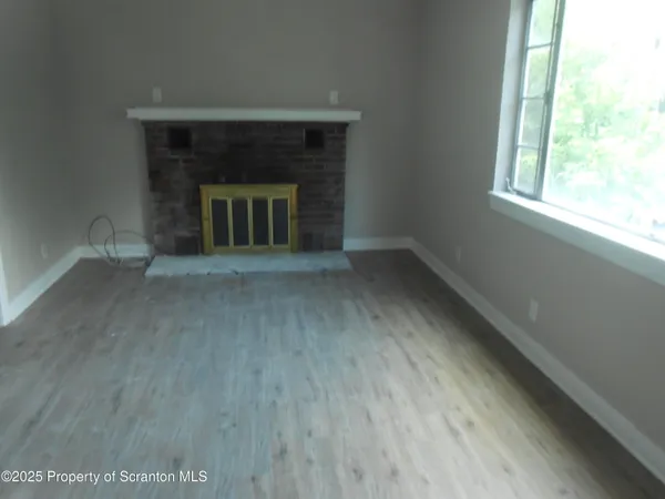 an empty room with wooden floor fireplace and windows