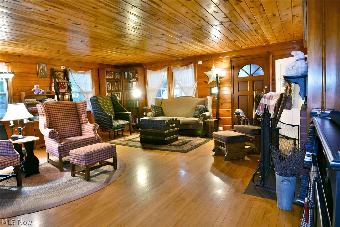 8683 King Graves Road Northeast Warren, OH 44484 - Photo 15 of 50 Living room featuring natural wood-paneled walls and ceiling, hardwood flooring, built-in bookshelves, and a paneled entry door with an arched window