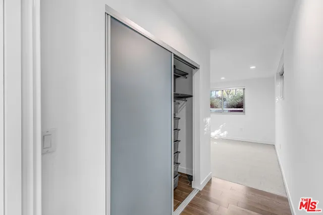 an empty room with wooden floor and way to kitchen