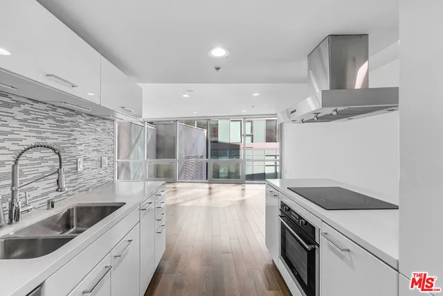 a kitchen with stainless steel appliances a sink dishwasher a refrigerator oven and white cabinets with wooden floor