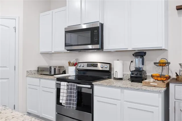 a kitchen with stainless steel appliances granite countertop white cabinets a stove a microwave and a sink