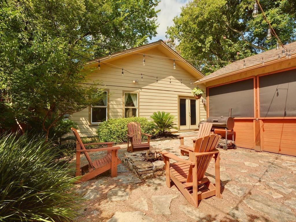 610 West N Loop Boulevard Austin, TX 78751 - Photo 24 of 29 The property features an inviting outdoor space with a stone-edged fire pit, surrounded by wooden Adirondack chairs, and string lights overhead