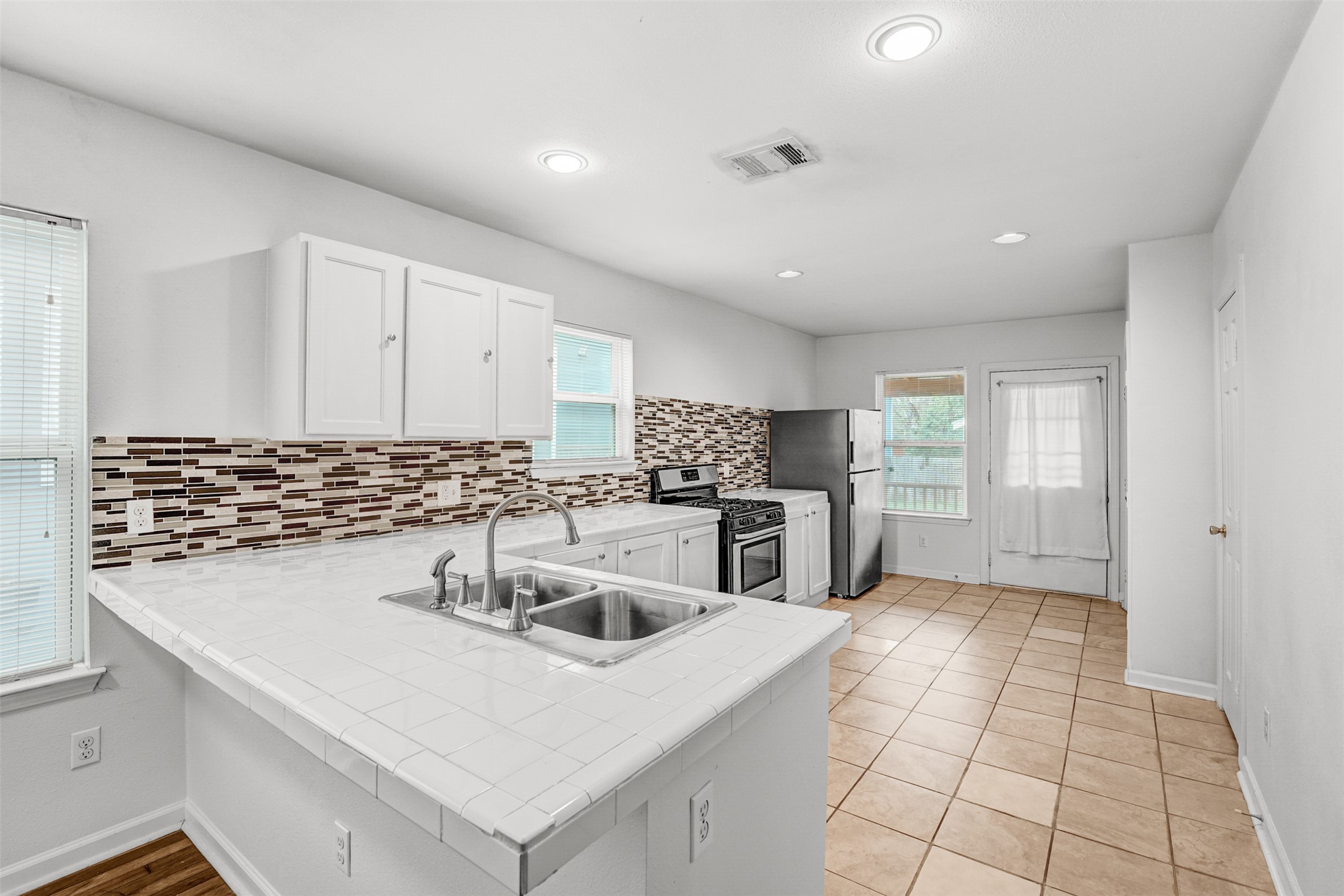 6906 Carver Avenue, Unit A Austin, TX 78752 - Photo 12 of 24 Kitchen with light countertops, stainless steel appliances, a peninsula, white cabinets, and backsplash