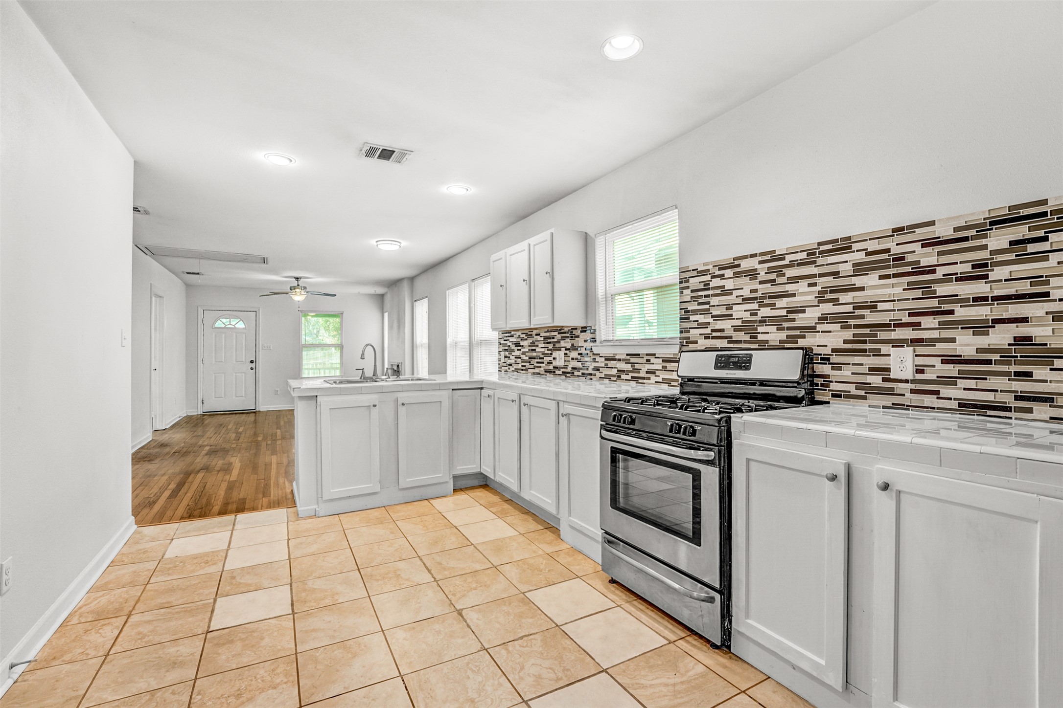 6906 Carver Avenue, Unit A Austin, TX 78752 - Photo 14 of 24 Kitchen with light tile patterned flooring, stainless steel range with gas cooktop, a peninsula, decorative backsplash, and white cabinetry