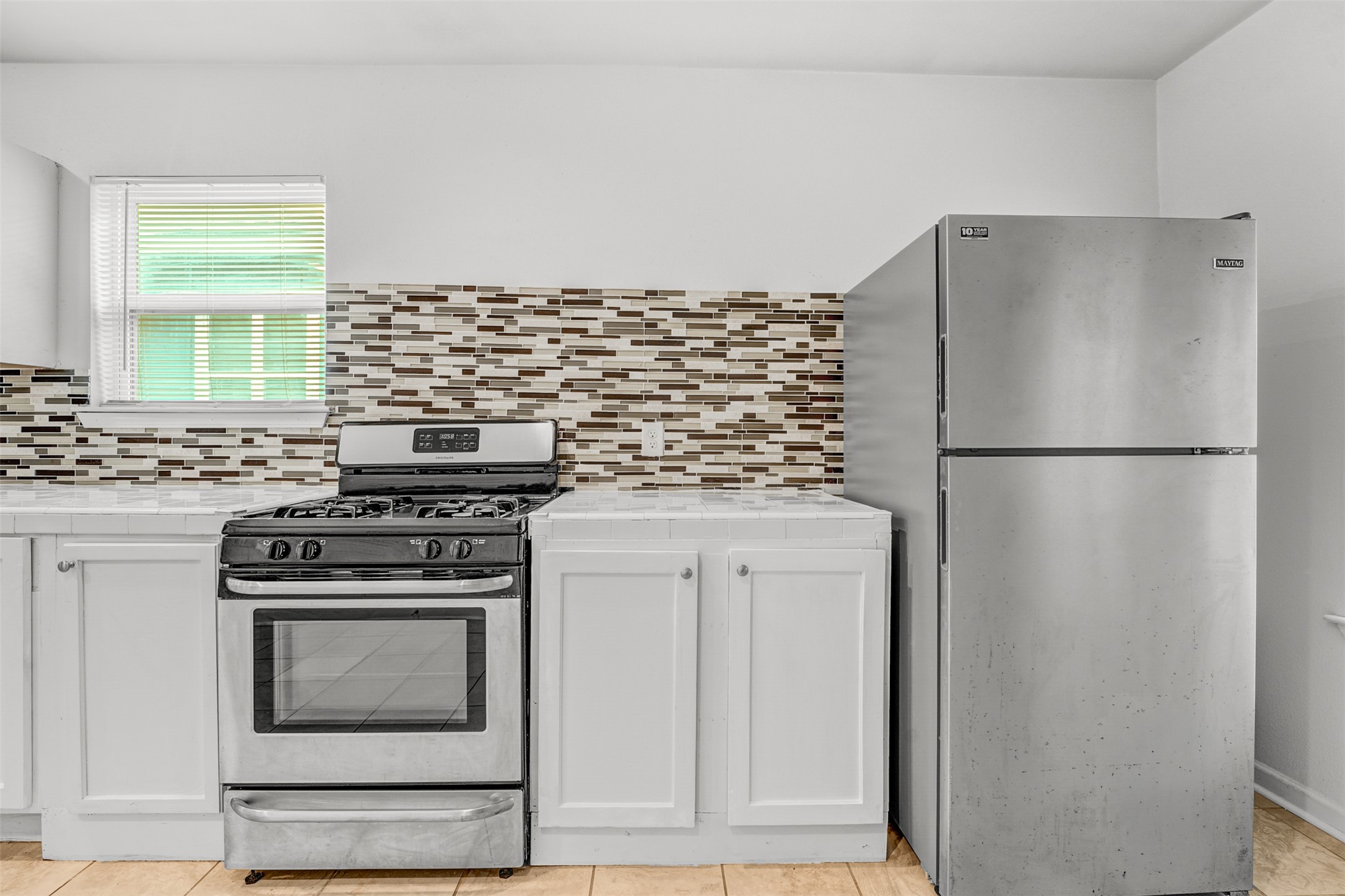 6906 Carver Avenue, Unit A Austin, TX 78752 - Photo 15 of 24 Kitchen featuring stainless steel appliances, tile countertops, light tile patterned flooring, white cabinetry, and decorative backsplash