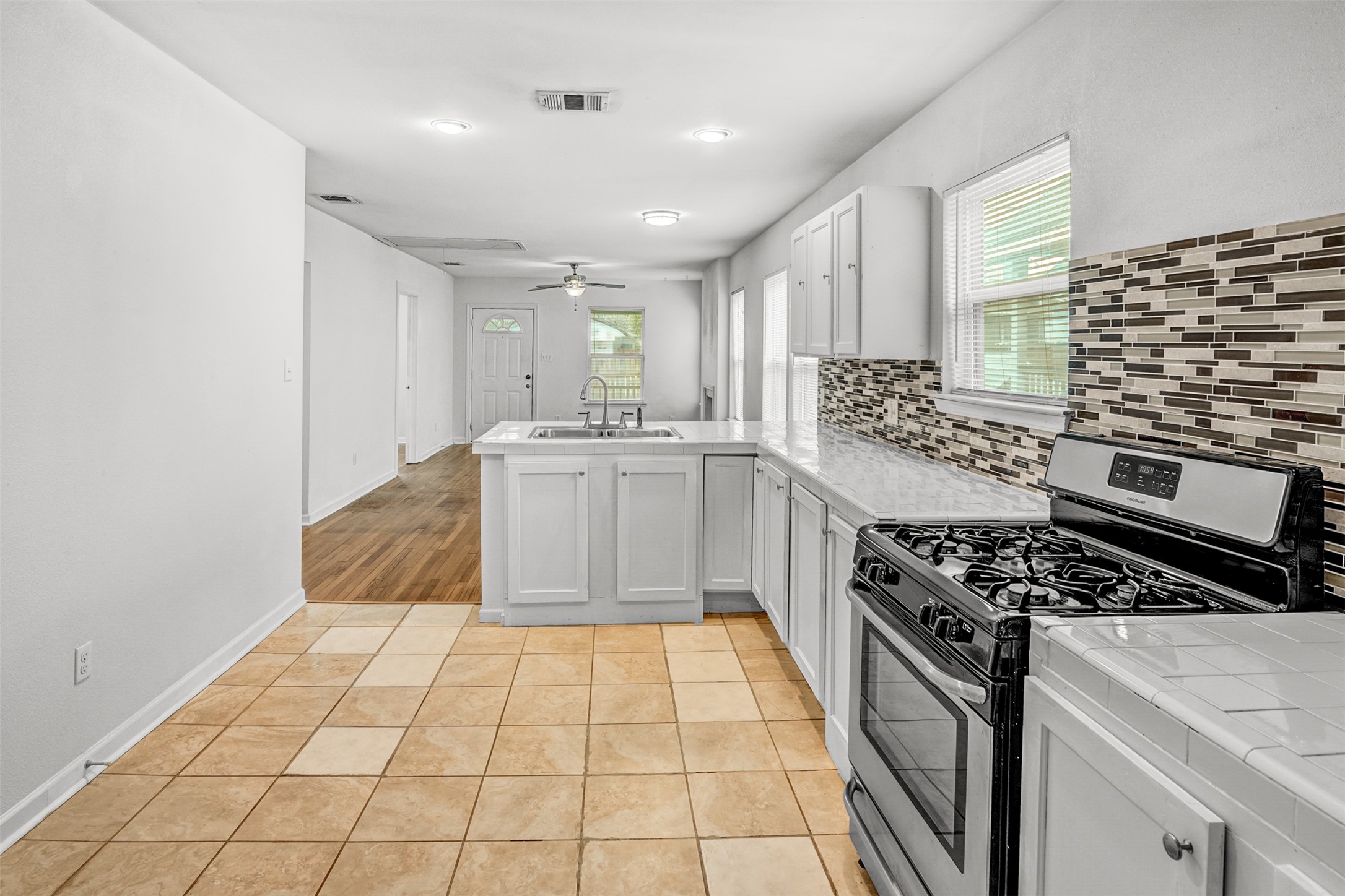 6906 Carver Avenue, Unit A Austin, TX 78752 - Photo 16 of 24 Kitchen featuring stainless steel gas stove, a peninsula, light tile patterned flooring, tile counters, and white cabinets