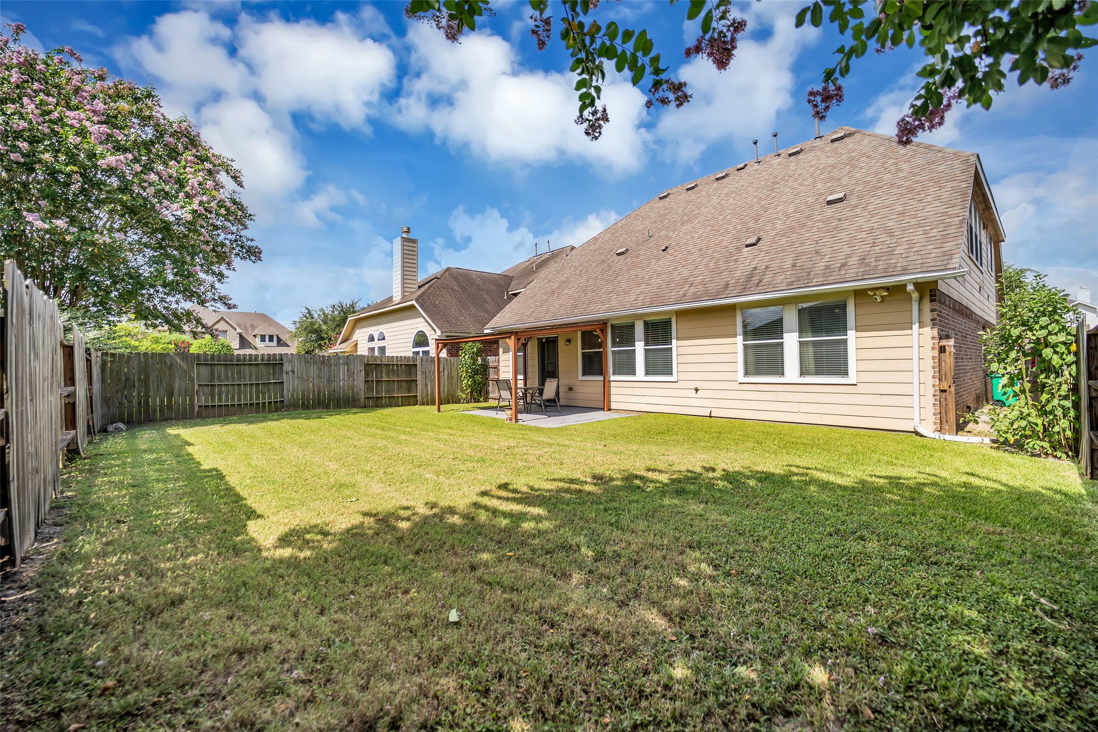5406 Quarry Ridge Road Richmond, TX 77407 - Photo 34 of 36 Large, fully fenced backyard offering generous green space for entertaining, outdoor activities, pets, or gardening. This angle showcases the covered patio, mature shade trees, and the home's rear elevation, creating an inviting outdoor setting with plenty of room to enjoy year-round.