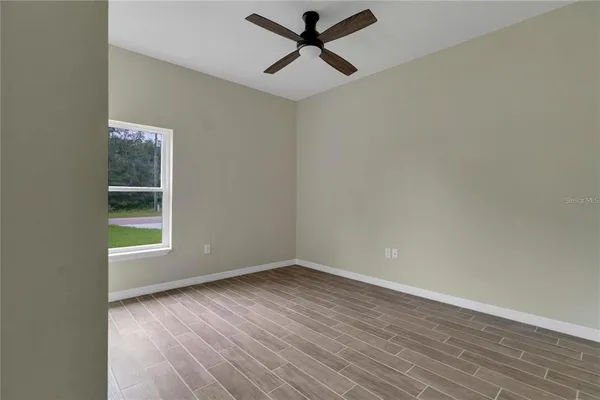 an empty room with wooden floor ceiling fan and windows