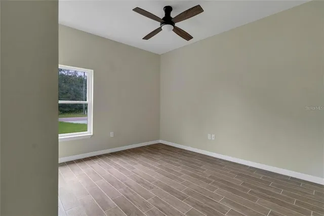 an empty room with wooden floor ceiling fan and windows