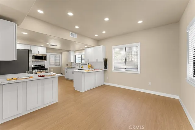 a kitchen with stainless steel appliances kitchen island granite countertop a stove a sink a refrigerator and white cabinets with wooden floor