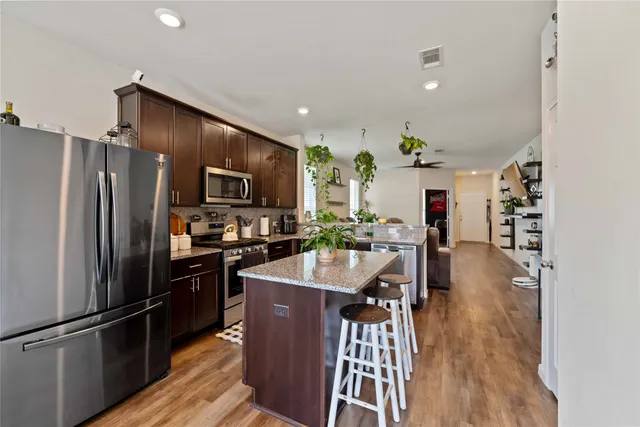 a kitchen with stainless steel appliances granite countertop a refrigerator a sink dishwasher a stove and a dining table with wooden floor