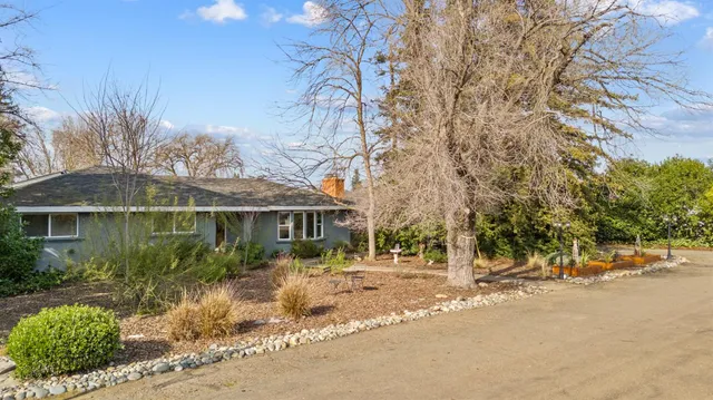 a view of a white house next to a road with large trees