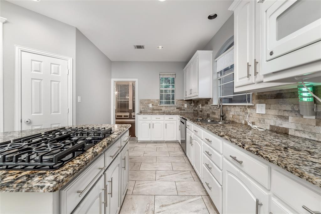 5801 Yeary Road Plano, TX 75093 - Photo 13 of 33 Galley kitchen featuring a gas range, stone countertops, white cabinetry with brushed nickel hardware, a stone tile backsplash, and light-toned tile flooring