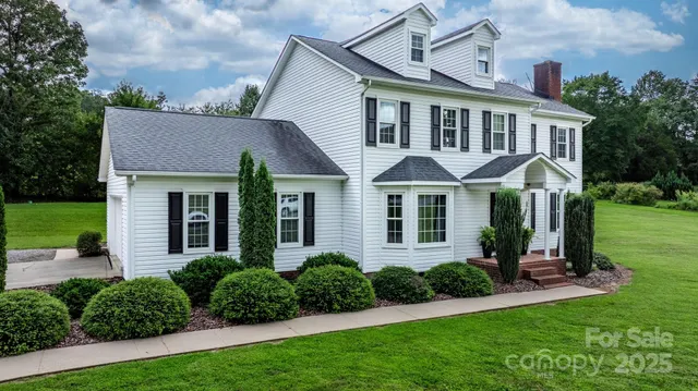 a view of a white house next to a yard with big trees