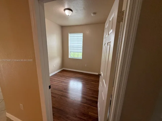 an empty room with wooden floor and windows with curtains