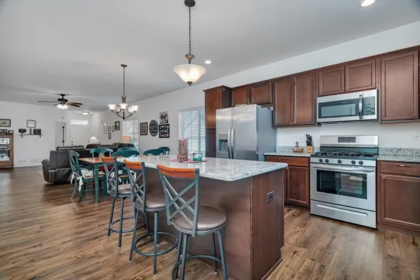 a kitchen with stainless steel appliances granite countertop a stove a refrigerator a kitchen island a dining table and chairs with wooden floor