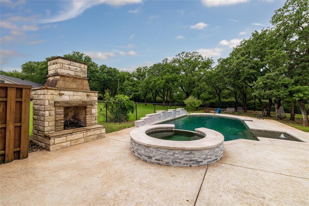 8948 David Fort Road Argyle, TX 76226 - Photo 36 of 39 Expansive outdoor patio featuring a built-in stone fireplace, a swimming pool with an integrated spa, and mature trees providing a natural backdrop