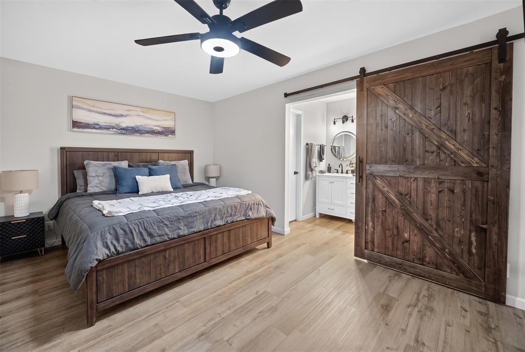 3919 Ridgeoak Way Farmers Branch, TX 75244 - Photo 14 of 28 Bedroom featuring wood-finish flooring, a ceiling fan with integrated lighting, and a dark wood barn door